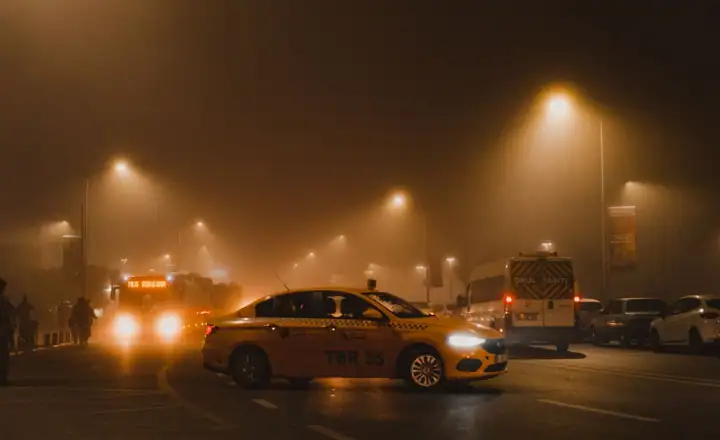 Sisli bir gecede farları yanan taksi