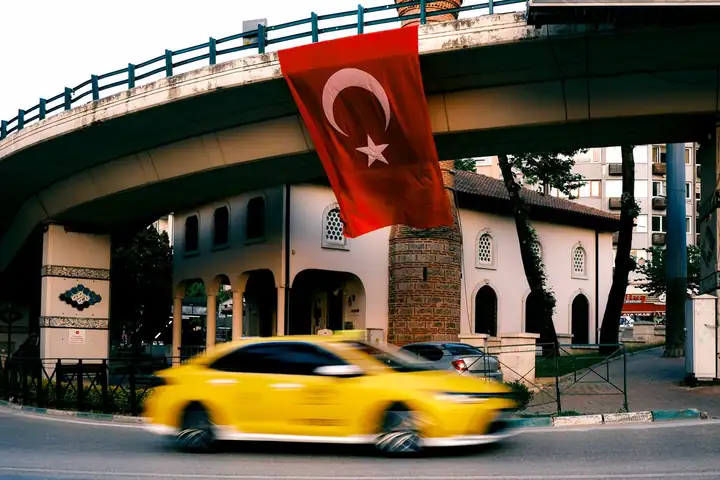 Türk bayraklı köprünün altından geçen sarı taksi